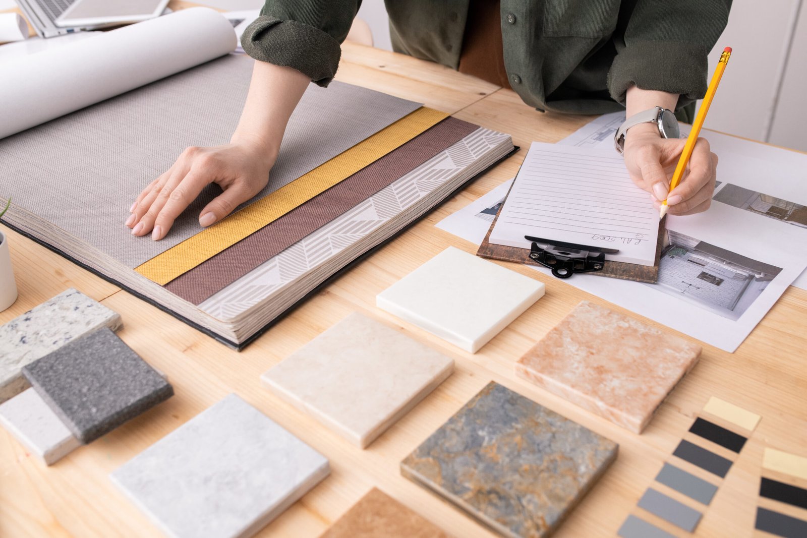 Hands of female interior designer with pencil over paper making notes Hands of female interior designer with pencil over paper making notes about color, pattern and texture of wallpapers for new client